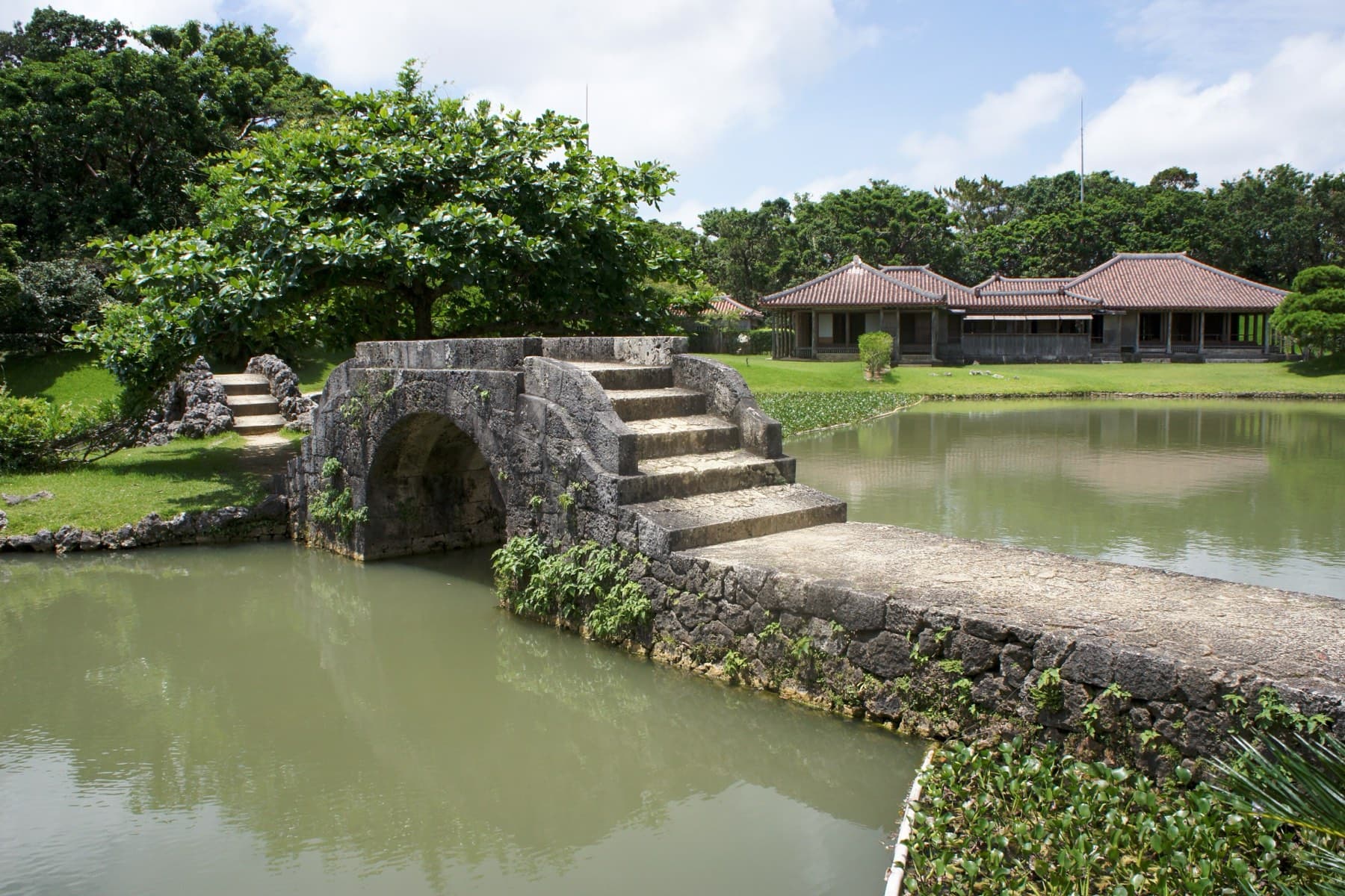 A limestone bridge with steps over its arch crosses the Shikinaen pond, and the wooden royal villa sits on the lawn across the water