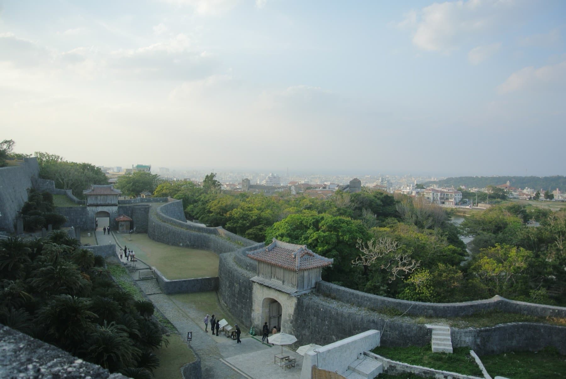 Late afternoon light falls on the walls and gates of Shuri Castle while the city of Naha spreads out to the horizon below