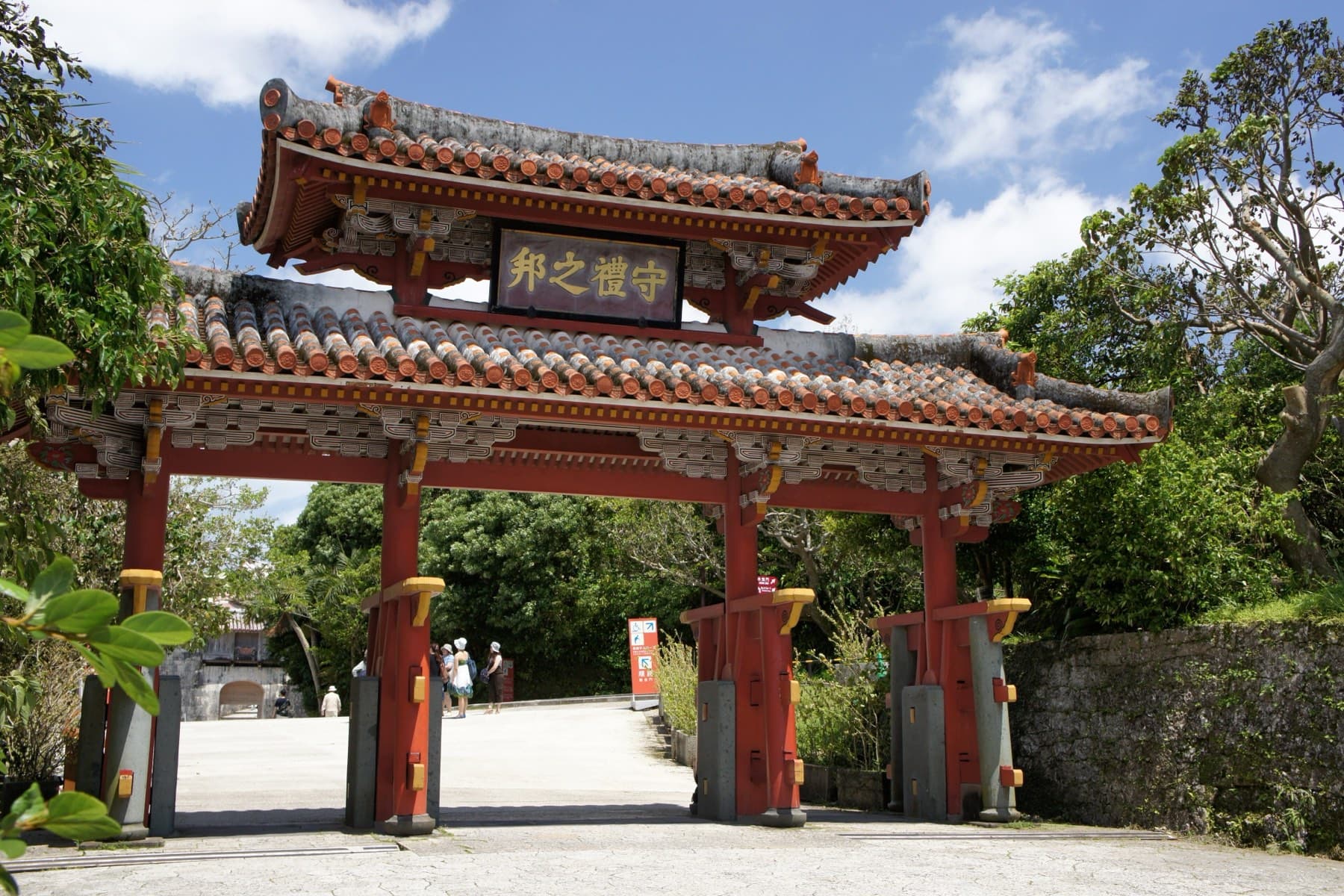 Shureimon gate stands on the approach to Shuri Castle in Naha, where red lacquered posts hold up two tiers of orange tile roof against a summer sky